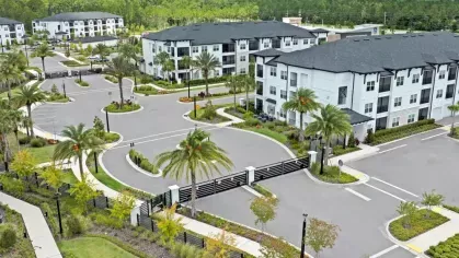 A bird’s-eye view of the gated entrance to the apartment community, featuring manicured landscaping and winding roads.
