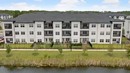 A closer aerial perspective of a lakeside apartment building with private balconies and a neatly maintained walking path.
