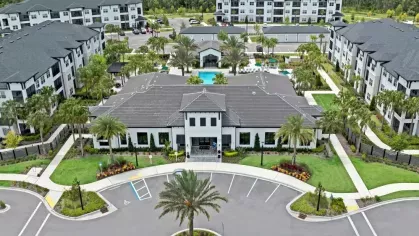 Overhead shot of a luxury apartment clubhouse entrance, surrounded by palm trees, landscaped gardens, and a resort-style swimming pool.