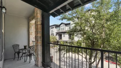 Private balcony with black wrought iron railing and views of the community surrounded by lush greenery.