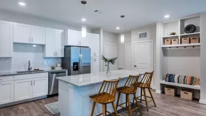 A modern kitchen featuring white cabinetry, stainless steel appliances, granite countertops, and pendant lighting over a spacious island with wooden barstools.