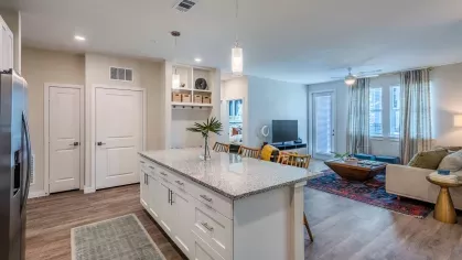 A modern kitchen featuring white cabinetry, stainless steel appliances, granite countertops, and pendant lighting over a spacious island with wooden barstools.