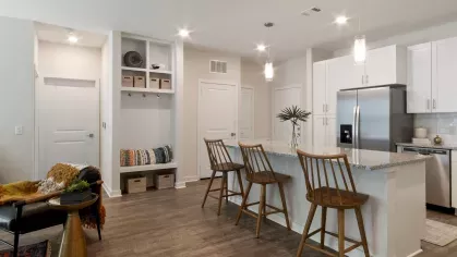 A modern kitchen featuring white cabinetry, stainless steel appliances, granite countertops, and pendant lighting over a spacious island with wooden barstools.