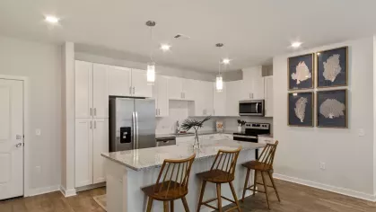 A modern kitchen featuring white cabinetry, stainless steel appliances, granite countertops, and pendant lighting over a spacious island with wooden barstools.