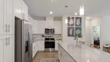 A modern kitchen featuring white cabinetry, stainless steel appliances, granite countertops, and pendant lighting over a spacious island with wooden barstools.