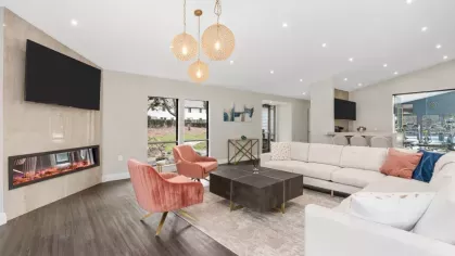 A modern lounge area with a large white sectional, pink accent chairs, a fireplace, and warm pendant lighting at Aurella Cary Apartments.