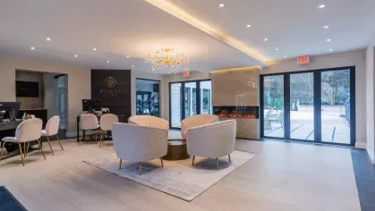 The leasing office at Aurella Cary Apartments with chic white chairs, a modern fireplace, and access to the pool area.