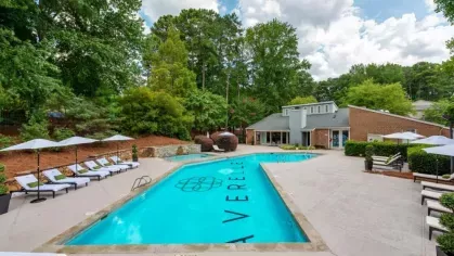 Resort-style swimming pool at Averelle North Hills surrounded by lounge chairs, umbrellas, and lush greenery.