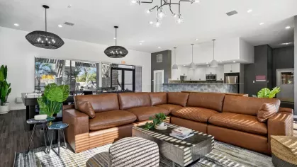 Spacious clubhouse with a large brown leather sectional, modern lighting, and a view into the kitchen.