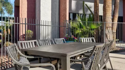 Outdoor dining area with a large table, metal chairs, and lush landscaping in the background.
