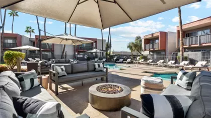 Outdoor lounge area with gray seating, fire pit, and poolside views under large umbrellas.