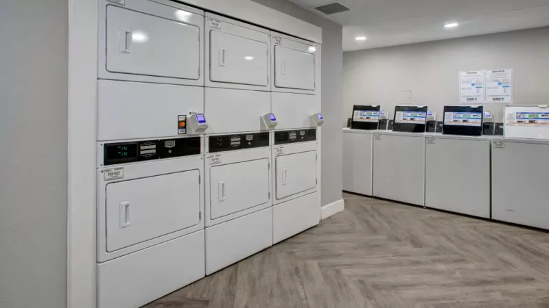 Laundry room with stacked white washers and dryers against a light gray wall, featuring modern payment systems.