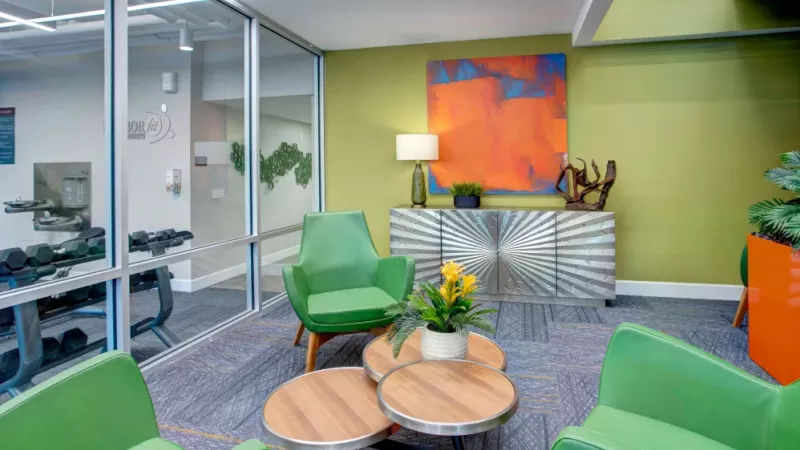 Colorful lounge area with vibrant green chairs, a metallic sunburst console, and a bold abstract painting against a lime green wall.