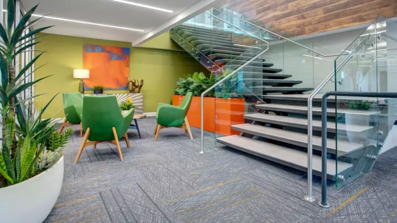 Bright and colorful lobby area with green accent chairs, vibrant artwork, and a glass staircase with a sleek design.
