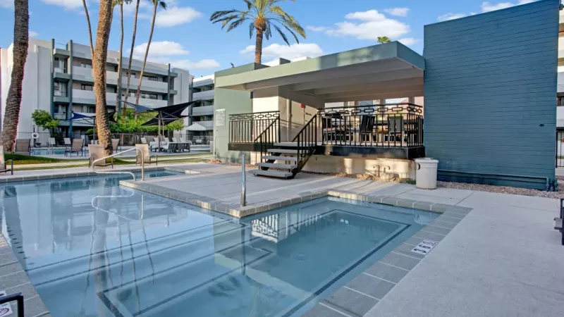 Crystal-clear pool with adjacent shaded seating and a modern building facade in the background.