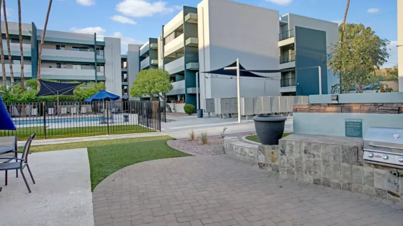 Outdoor community area featuring a built-in stainless steel grill, modern seating, and landscaped grounds.