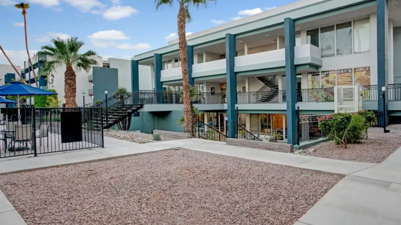 Ground-level view of the apartment complex with a fenced seating area and vibrant landscaping.