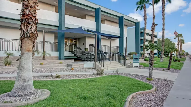 Front entrance of the building featuring a shaded canopy, well-maintained greenery, and a modern stairway.