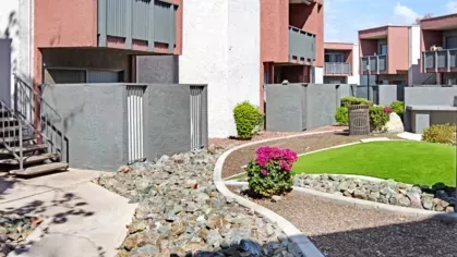 Modern apartment building with red and white exterior and landscaped pathways with rocks and greenery.