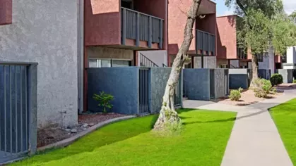 Apartment complex with red and gray buildings surrounded by lush green lawns and mature trees.