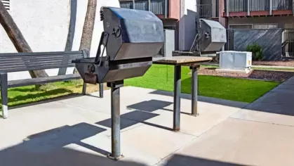 Outdoor grilling station with metal barbecue grills and a shaded seating area in a well-maintained courtyard.