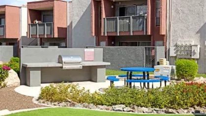 Outdoor picnic and barbecue area with a stainless steel grill and vibrant blue picnic tables.