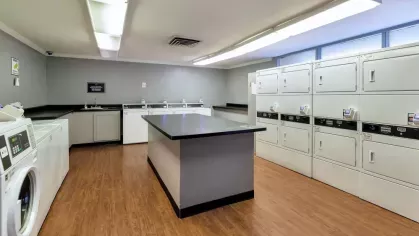 Bright and clean laundry room with multiple washers, dryers, and a central folding station.