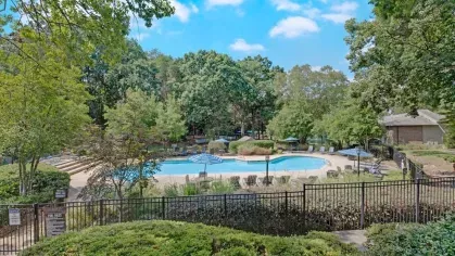 A serene pool surrounded by lush greenery and lounge chairs under blue umbrellas.