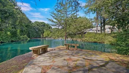 A peaceful pond with a stone-paved seating area and a view of surrounding trees.