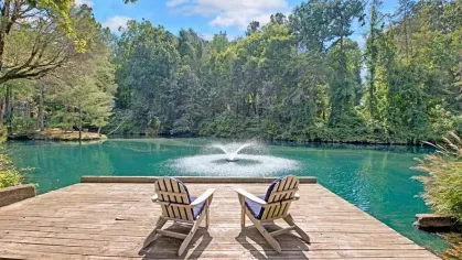 A wooden deck with Adirondack chairs overlooking a tranquil pond with a fountain.