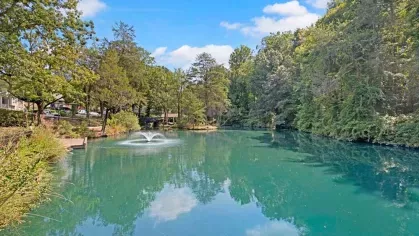 A picturesque pond with a central fountain, surrounded by vibrant green trees.
