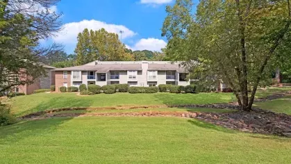 A charming apartment building with a well-maintained lawn and surrounding greenery.