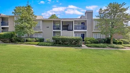 An apartment complex with light gray siding, dark blue balconies, and neatly trimmed bushes.