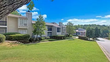 A row of modern apartment buildings with a wide, green lawn and a serene suburban setting.