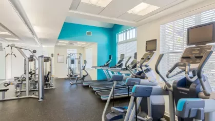 A bright fitness center with various cardio machines and weightlifting equipment against a turquoise accent wall.
