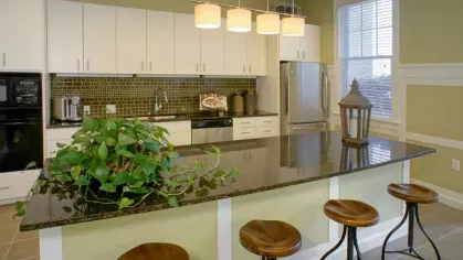 A chic kitchen with a black granite island, bar stools, and warm pendant lighting, complemented by white cabinetry.