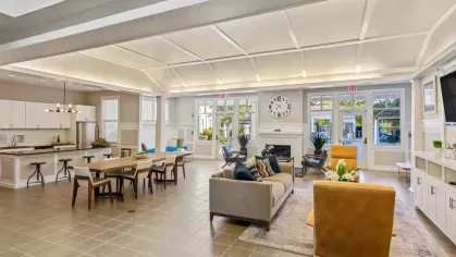 A wide-angle view of a community clubhouse showcasing a kitchen, dining, and lounge area with bright, natural lighting.