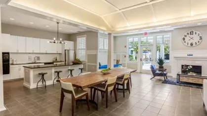 A bright kitchen space featuring white cabinets, a large island with barstools, and contemporary lighting fixtures.