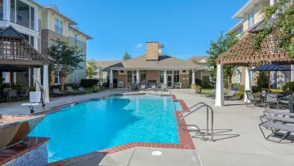 A view of a swimming pool with adjacent apartment buildings and a pergola providing a shaded retreat.