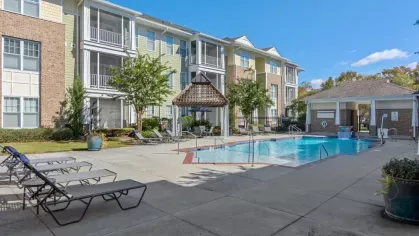 A serene poolside area with lounge chairs, a shaded pergola, and nearby apartments.