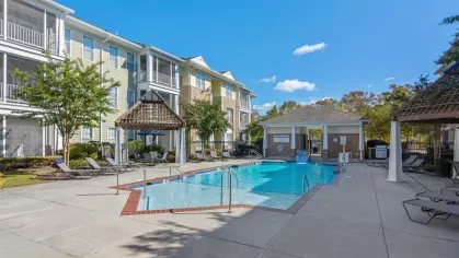 A clubhouse building with a peaked roof, two flags flanking the entrance, and manicured landscaping.