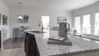 A view from the kitchen island looking into a dining and living area with large windows and glass doors letting in natural light.