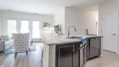 A bright and spacious open living area with a view of the kitchen and dining spaces, featuring a double sink on the island.