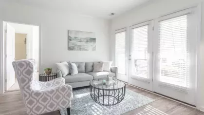 A bright living room with glass doors opening to a patio or balcony, with a circular coffee table and decorative rug.