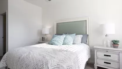 A neatly decorated bedroom with a headboard, white linens, and matching nightstands on either side of the bed.