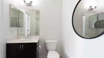 A clean bathroom with a dark wood vanity, a large round mirror, and a bright white sink and toilet.