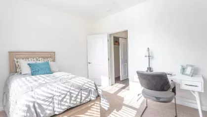 A bright guest room or office space with a single bed, a desk, and natural light streaming in through the windows.