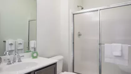 A clean bathroom with a glass-enclosed shower, a modern vanity with a large mirror, and neatly arranged white towels.