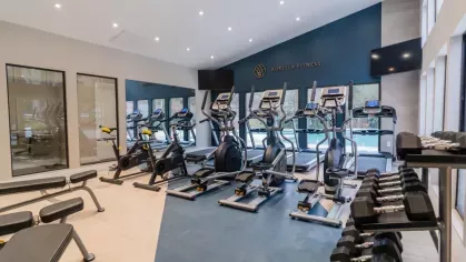 A well-equipped fitness center with cardio machines, free weights, and large windows at Aurella Cary Apartments.