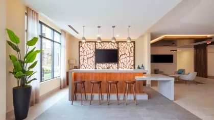 The Everly's sleek resident bar area, featuring a white quartz counter, pendant lighting, and a striking geometric accent wall with a mounted TV.